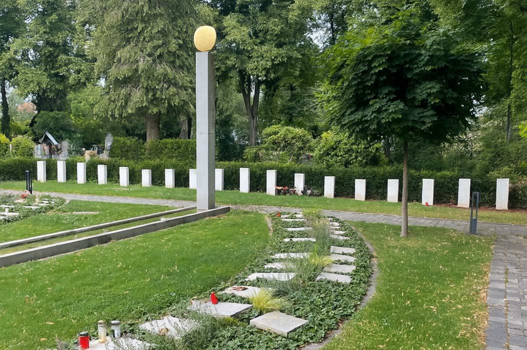 Eine friedliche Grünanlage mit Steinstelen und einem hohen Denkmal mit goldener Kugel inmitten.
