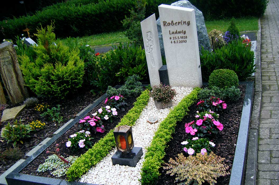 Ein gepflegtes Grab mit Blumen und einer Grabsteininschrift bei bewölktem Wetter.