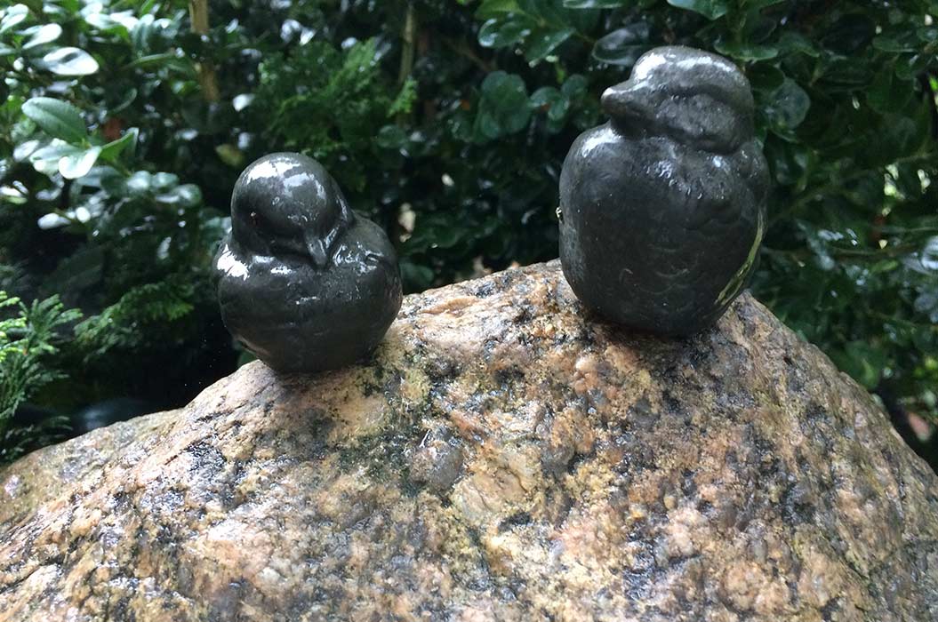 Zwei Vogelstatuen aus dunklem Stein auf einem Felsen in einem grünen Garten.