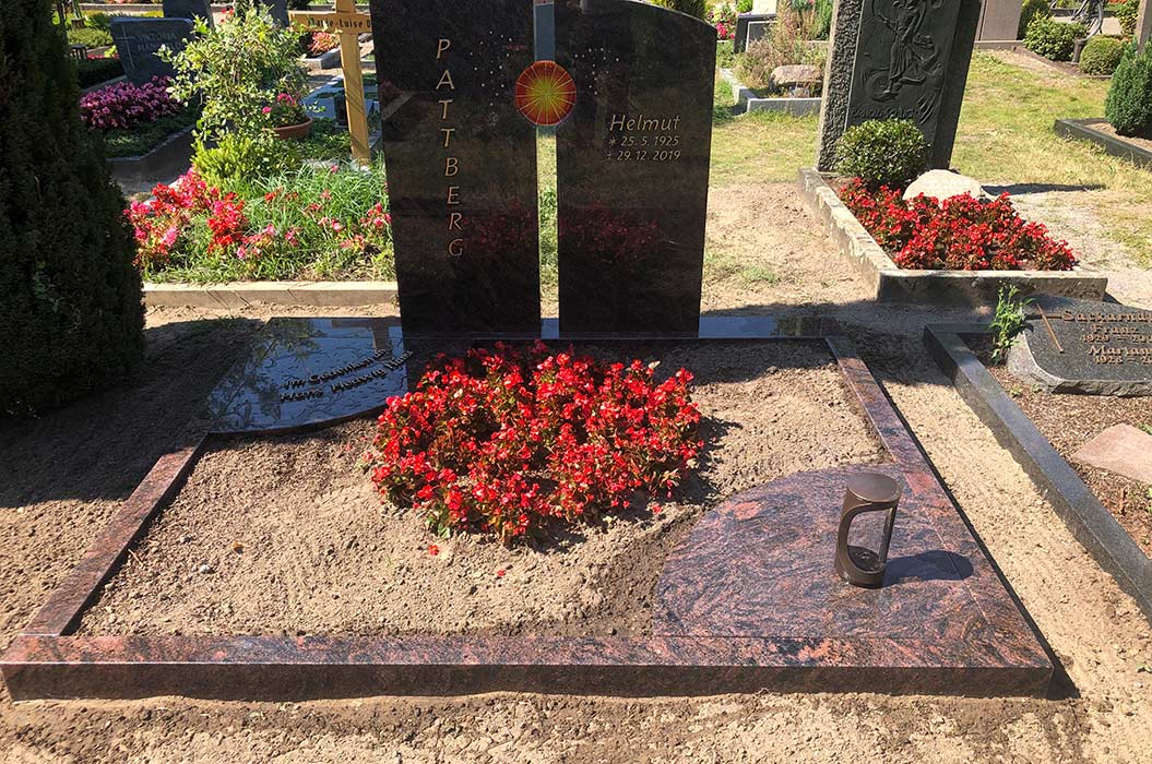 Grabstein mit der Aufschrift "Pattberg Helmut", umgeben von Blumen und Kerzen auf einem Friedhof.