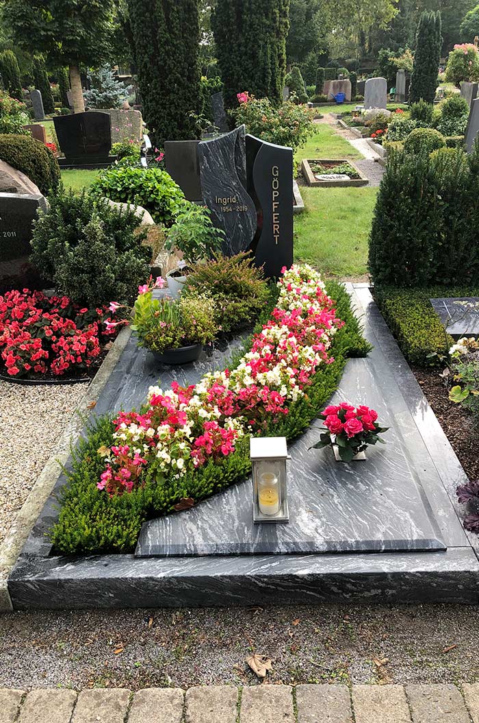 Grabstein mit Blumenarrangement, rote und weiße Blüten, Laterne vorne, friedlicher Friedhof.