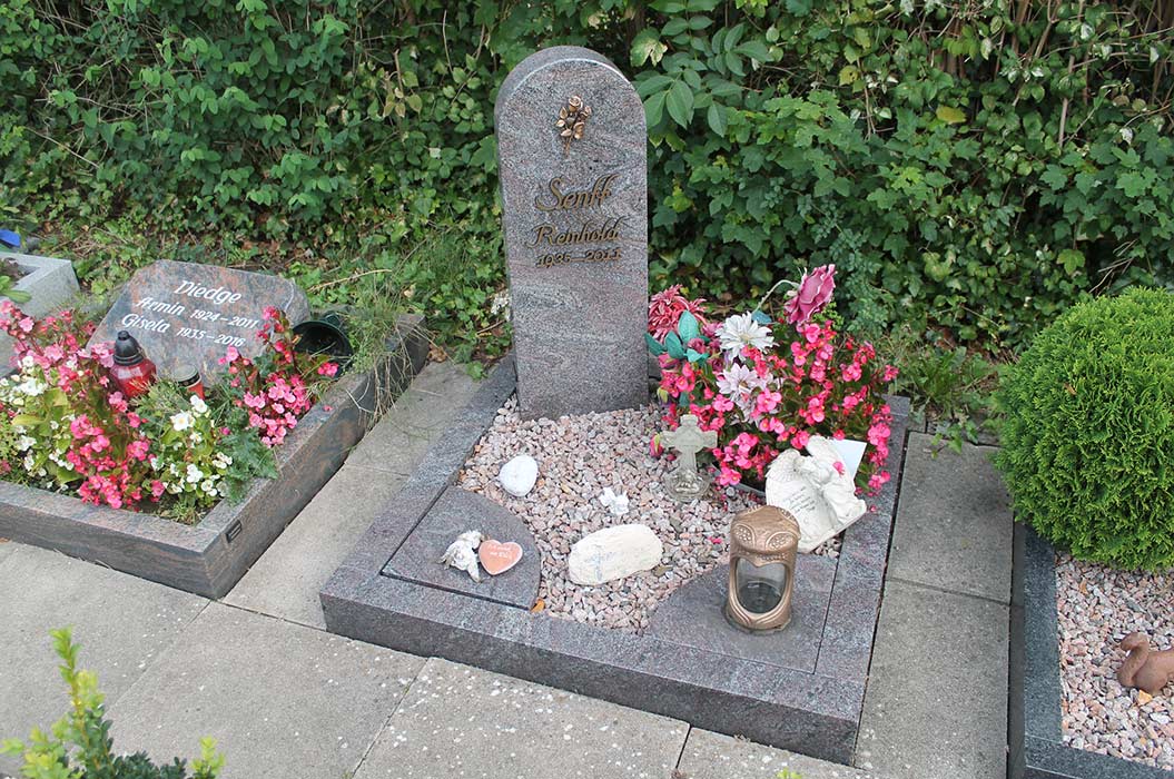 Ein Grab mit einem grauen Grabstein, umgeben von bunten Blumen und Dekorationen.