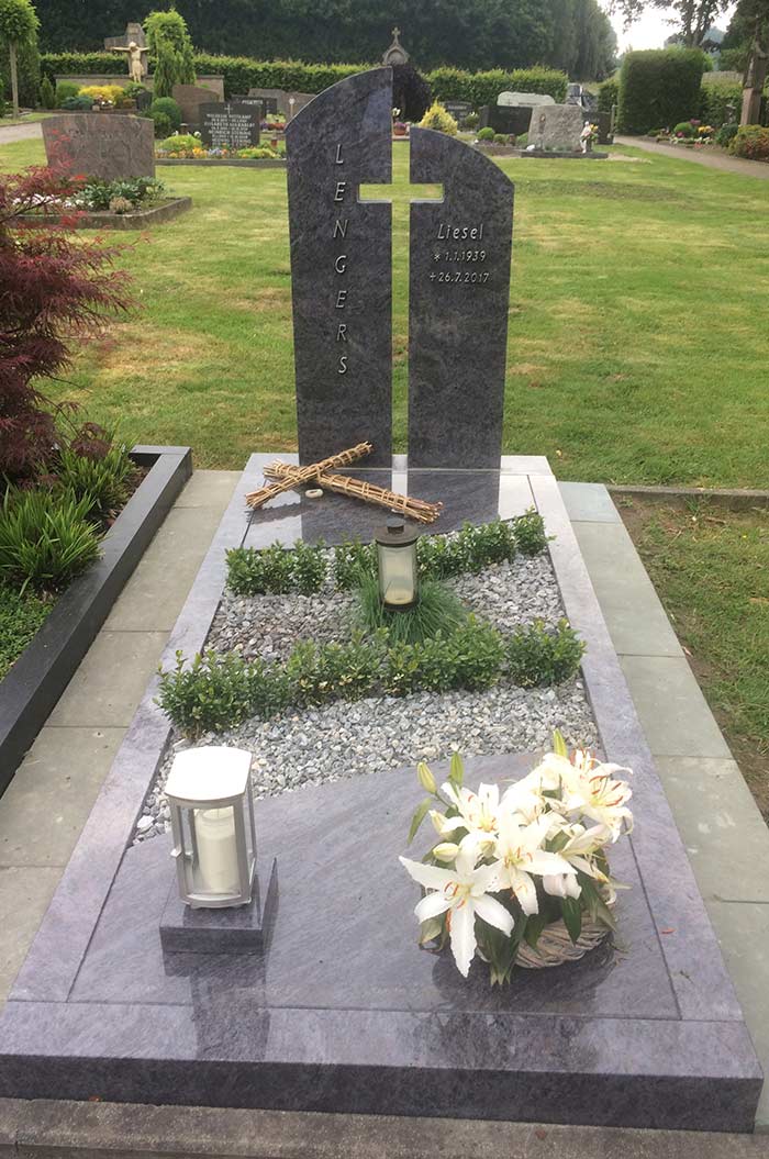 Grabstein auf einem Friedhof mit Blumen und Kerzen, umgeben von gepflegtem Rasen.