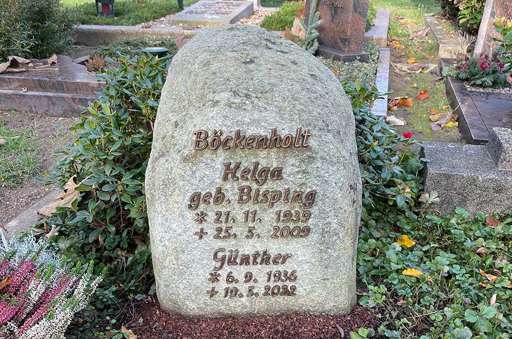 Grabstein mit Inschrift für Helga und Günther Böckenholt, umgeben von herbstlichem Laub und Blumen.