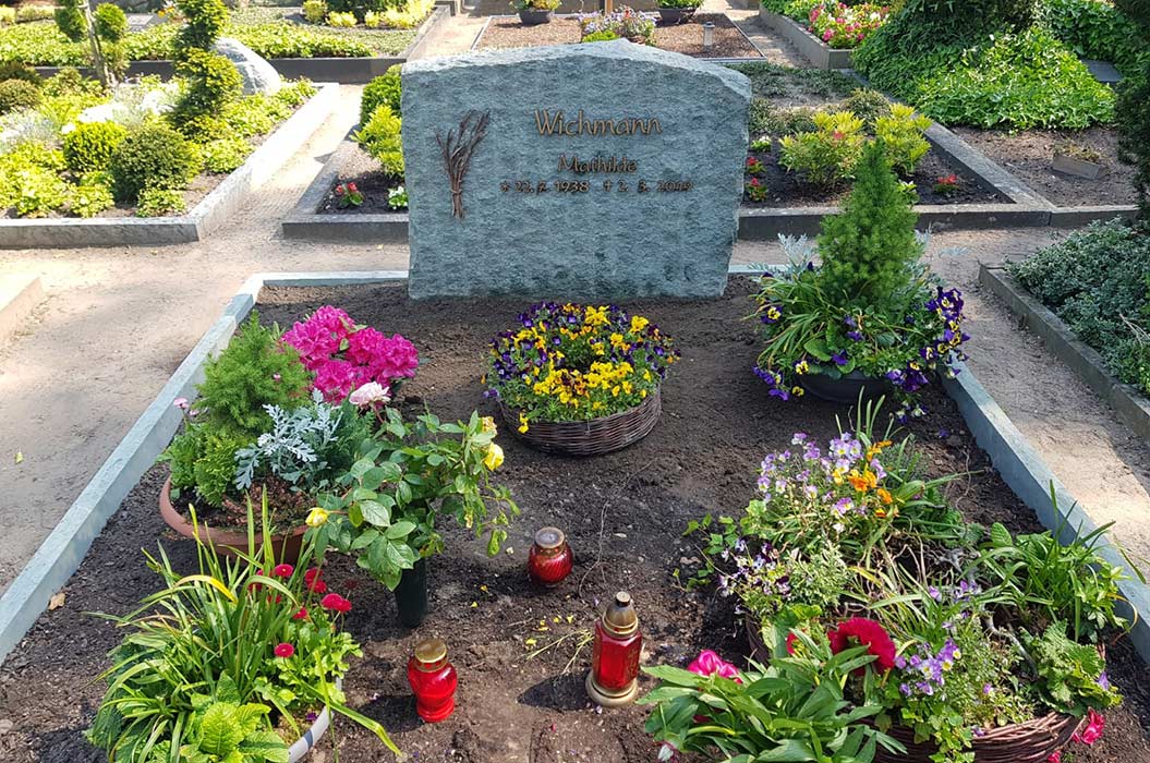 Grab mit Blumenarrangement, bunter Blumenschmuck, Grabstein mit Gravur. Ruhige Friedhofsatmosphäre.