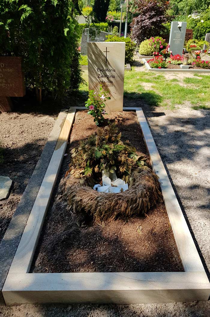 Ein gepflegtes Grab mit Grabstein, blühenden Blumen und einem umrandeten Bereich auf einem Friedhof.