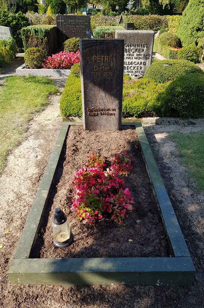 Grabstein von Dieter Petri (1950-2019) mit Blumen und einer Kerze auf einem gepflegten Friedhof.