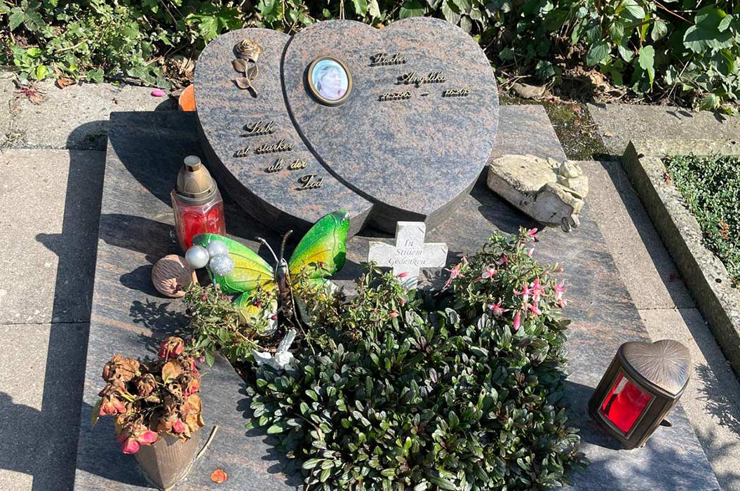 Ein Grabstein mit Blumen, Schmetterlingsdeko und roten Laternen auf einem Friedhof.
