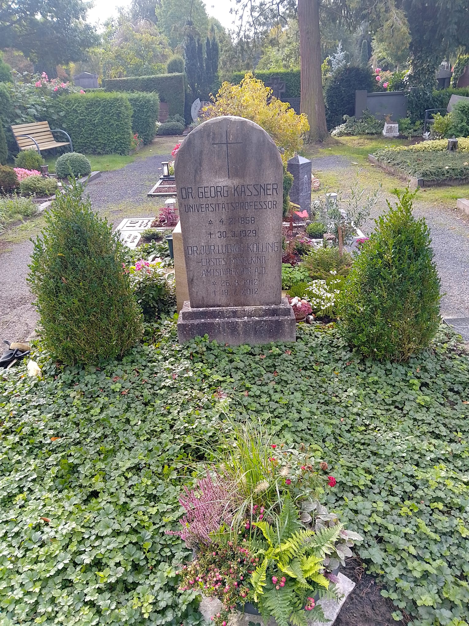 Grabstein von Dr. Georg Kassner auf einem gepflegten Friedhof mit bunten Blumen