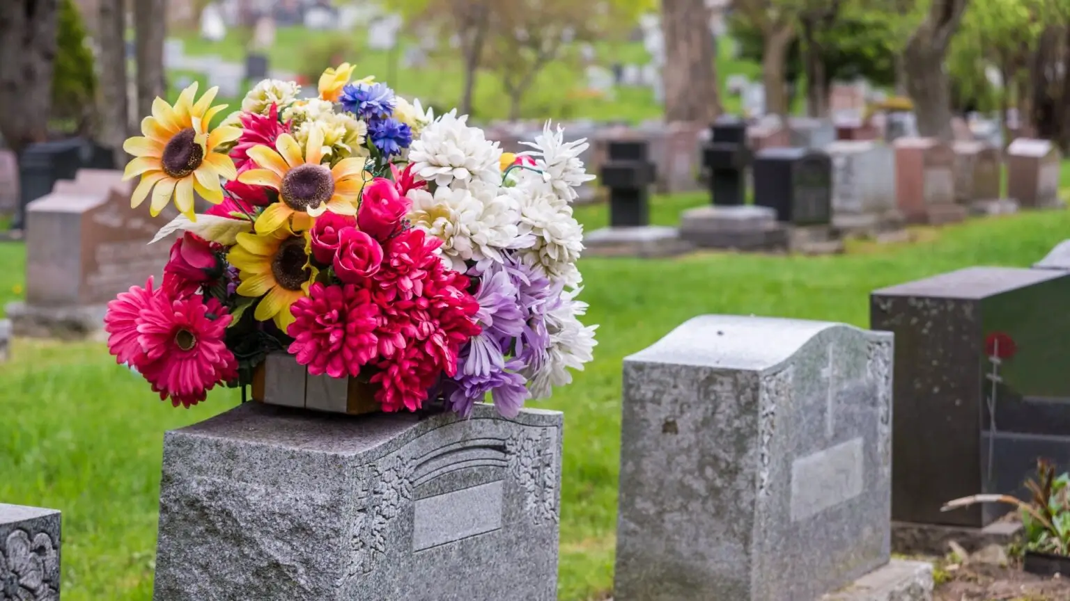 Ein bunter Strauß aus gelben, roten und weißen Blumen liegt auf einem Grabstein